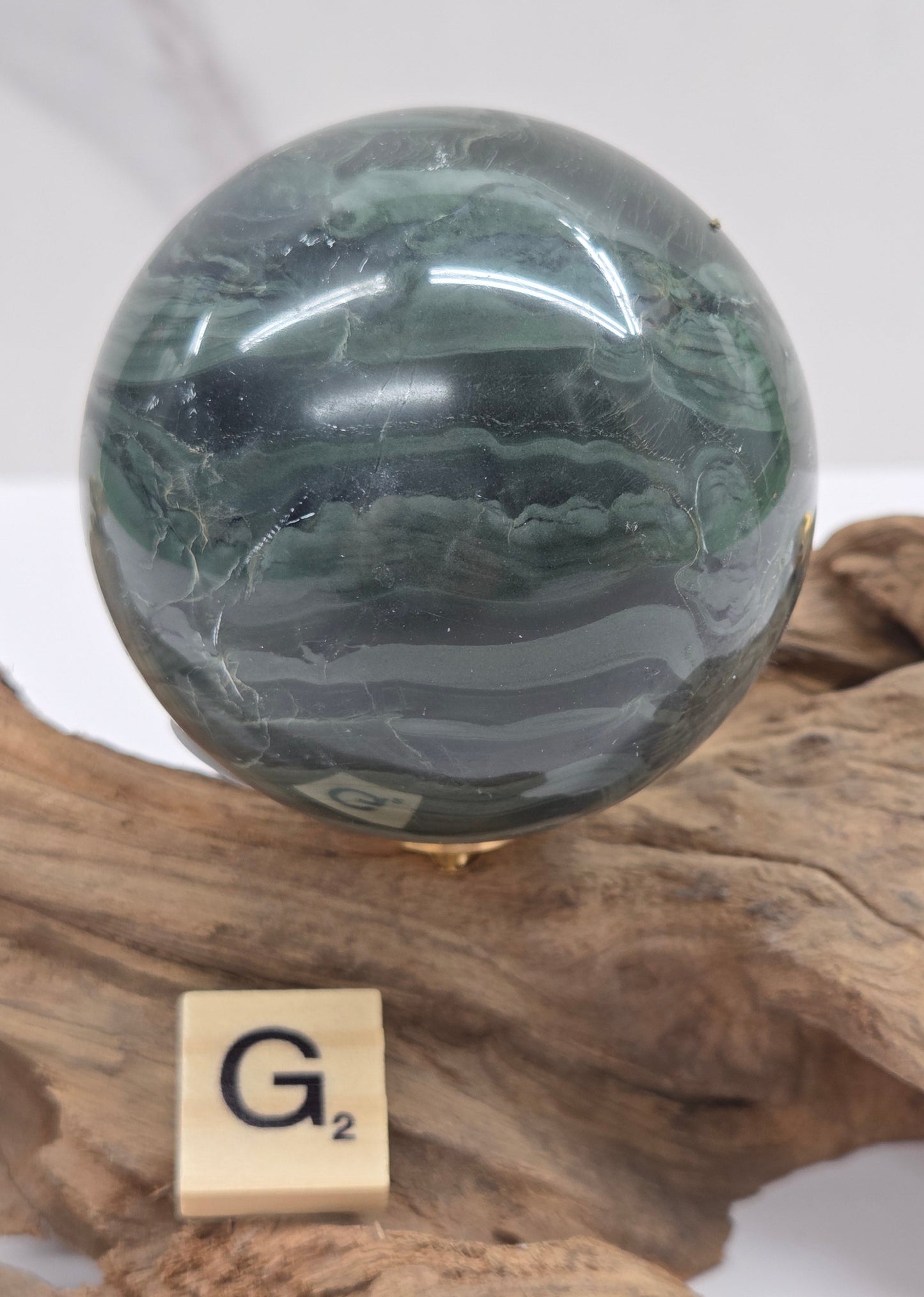 Green wave picture jasper sphere with a wave like pattern, on a driftwood stand, on a white background