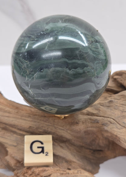 Green wave picture jasper sphere with a wave like pattern, on a driftwood stand, on a white background