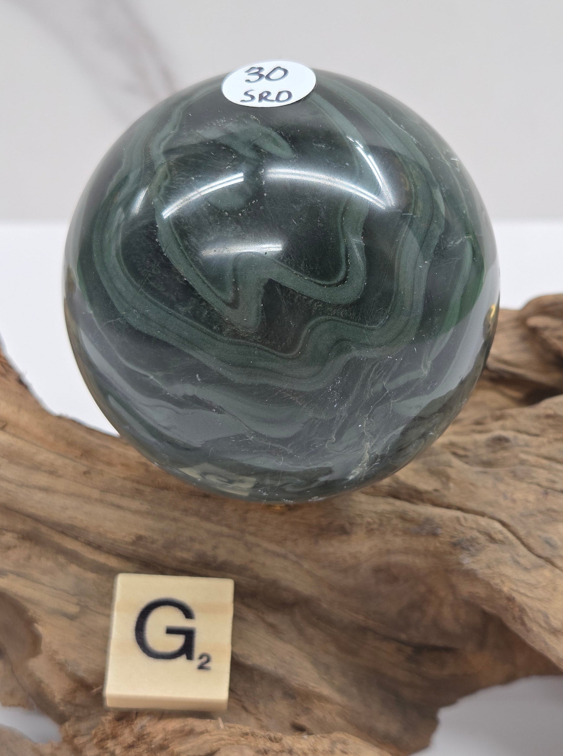 Green wave picture jasper sphere with a wave like pattern, on a driftwood stand, on a white background