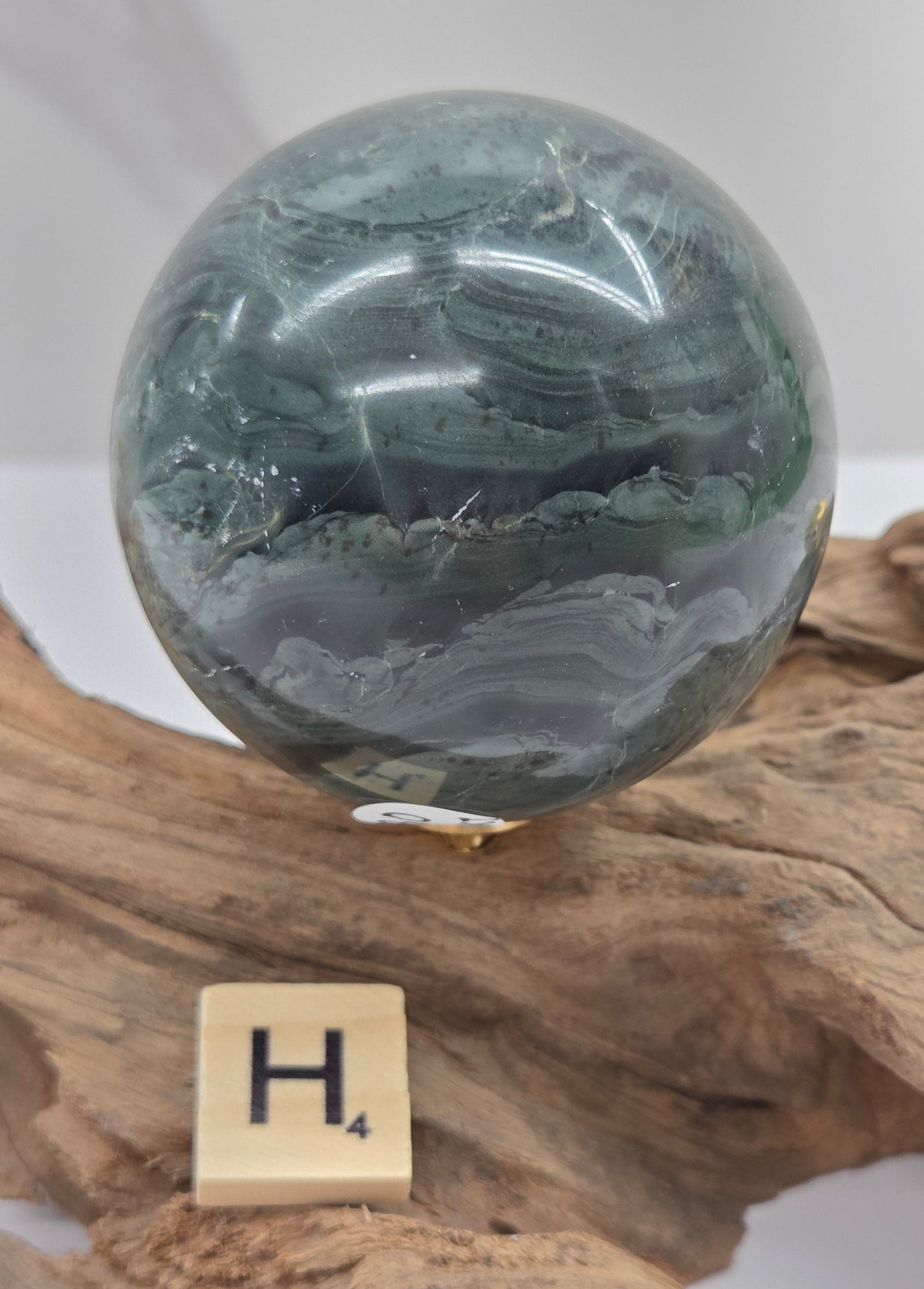 Green wave picture jasper sphere with a wave like pattern, on a driftwood stand, on a white background