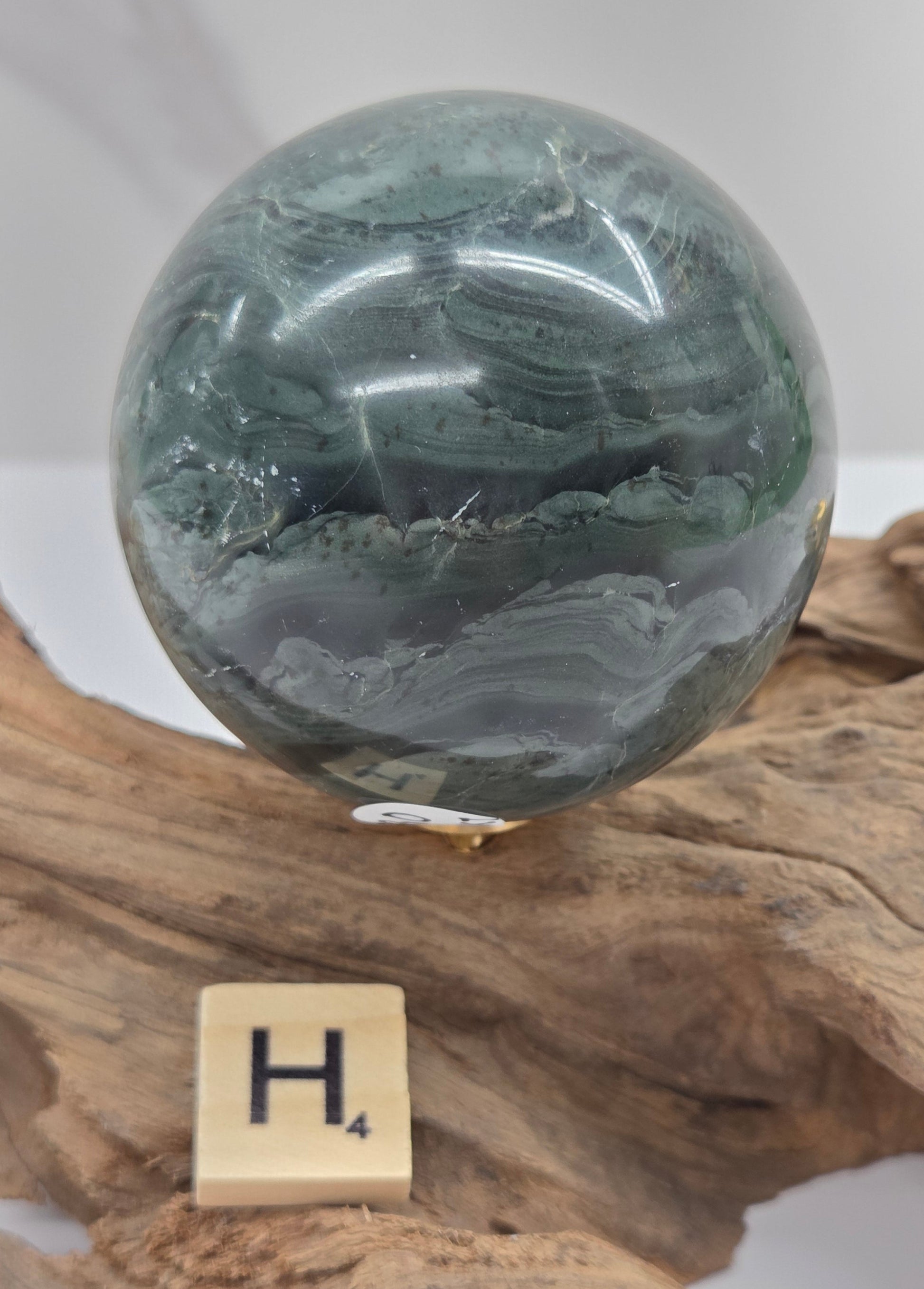 Green wave picture jasper sphere with a wave like pattern, on a driftwood stand, on a white background