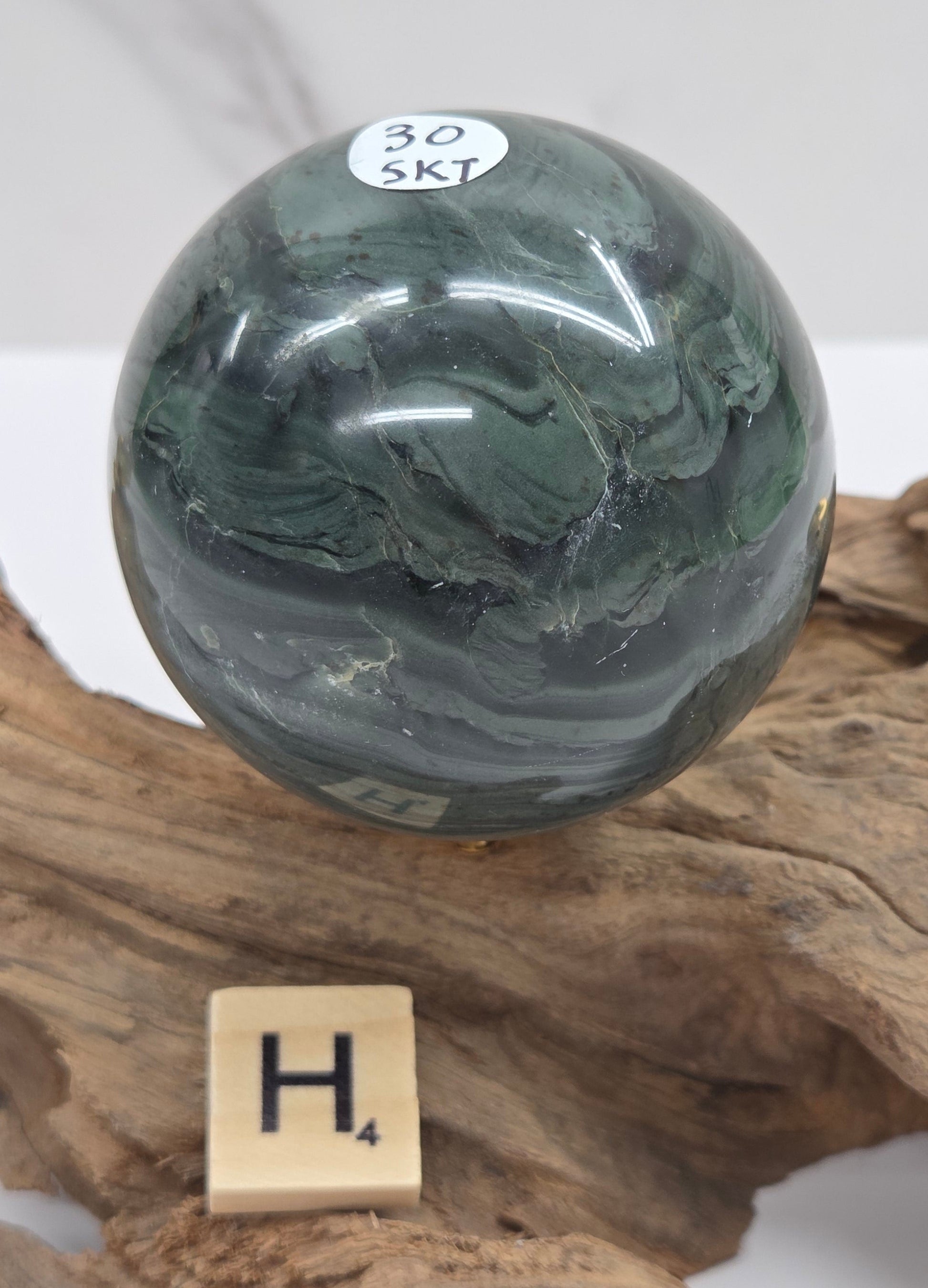 Green wave picture jasper sphere with a wave like pattern, on a driftwood stand, on a white background