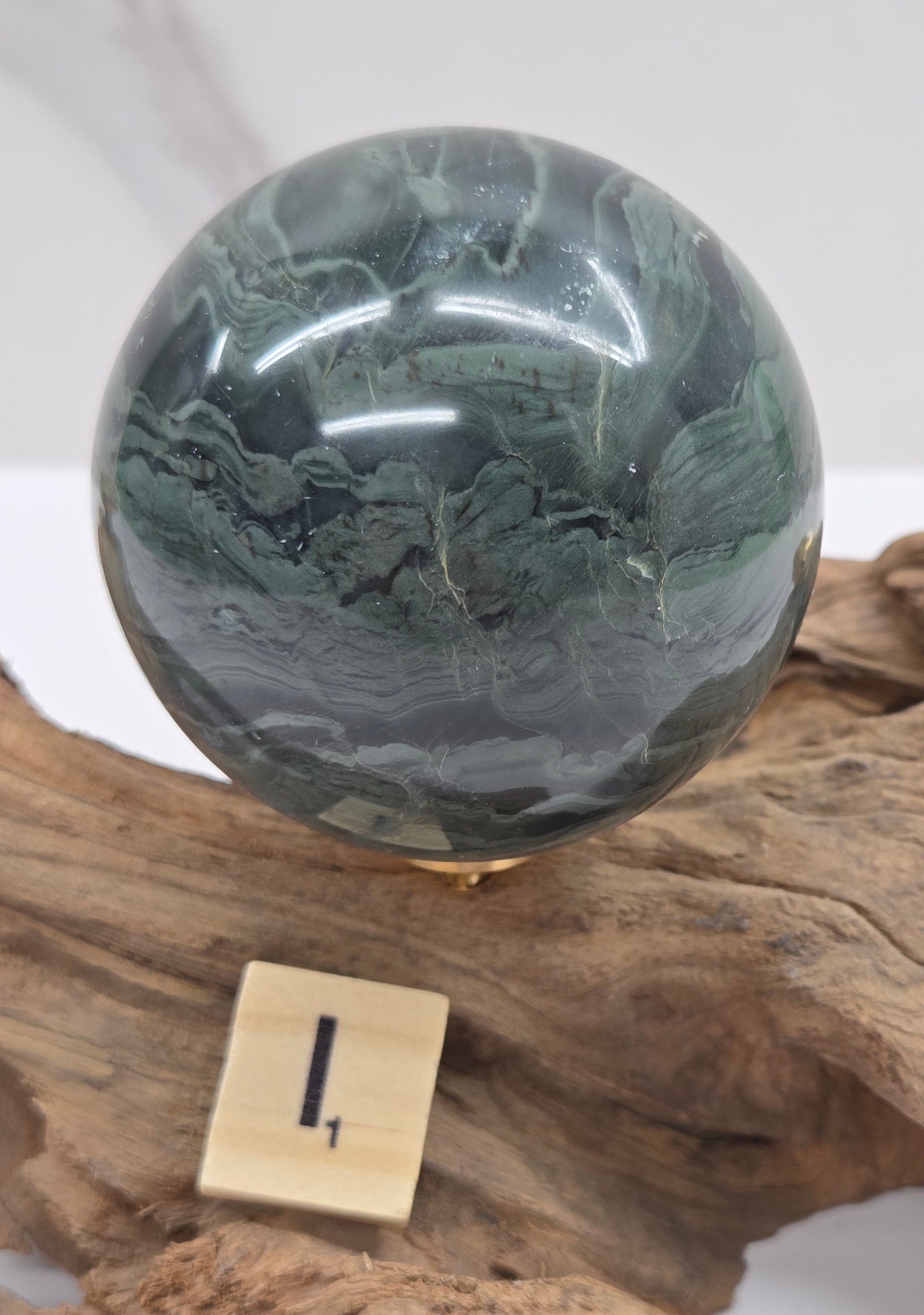 Green wave picture jasper sphere with a wave like pattern, on a driftwood stand, on a white background