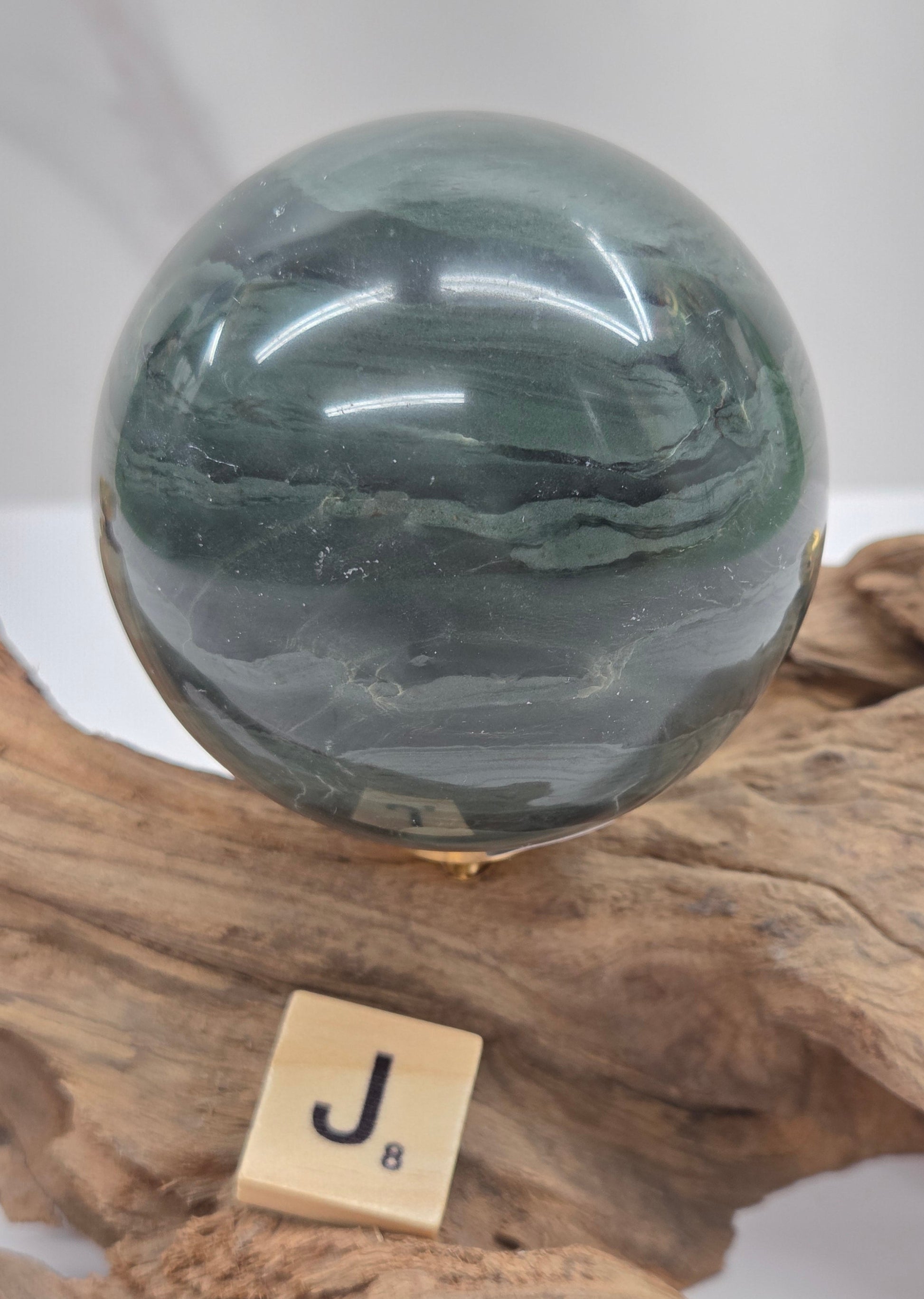 Green wave picture jasper sphere with a wave like pattern, on a driftwood stand, on a white background