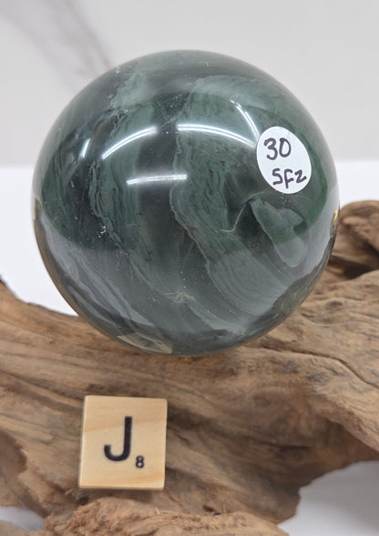 Green wave picture jasper sphere with a wave like pattern, on a driftwood stand, on a white background