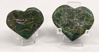 Set of 2 emerald hearts with yellow and black inclusions, on display stands on a white background