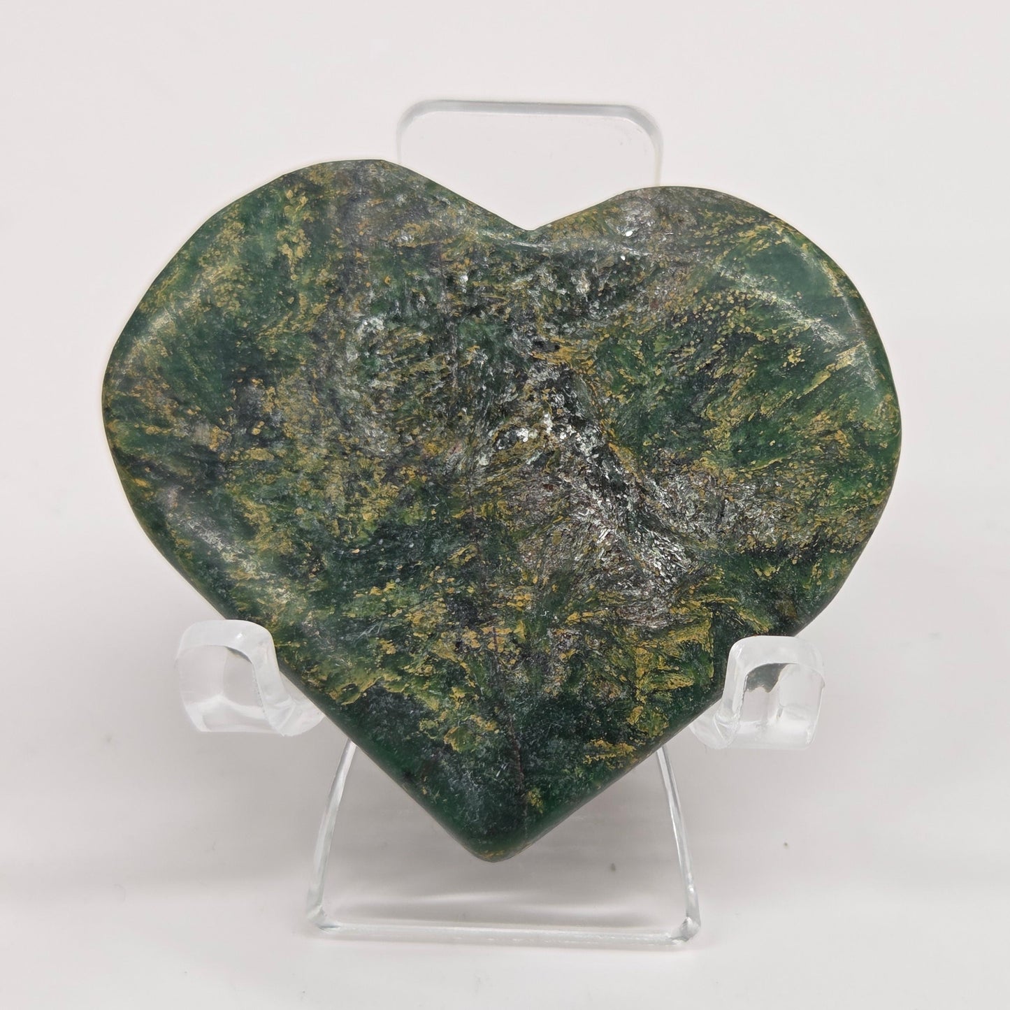 Emerald heart with yellow and black inclusions, on a display stand on a white background