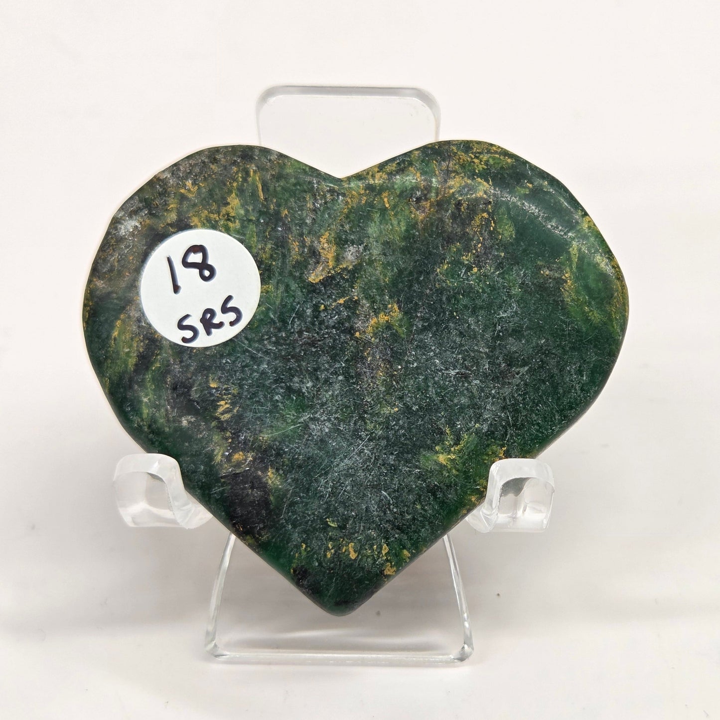 Emerald heart with yellow and black inclusions, on a display stand on a white background