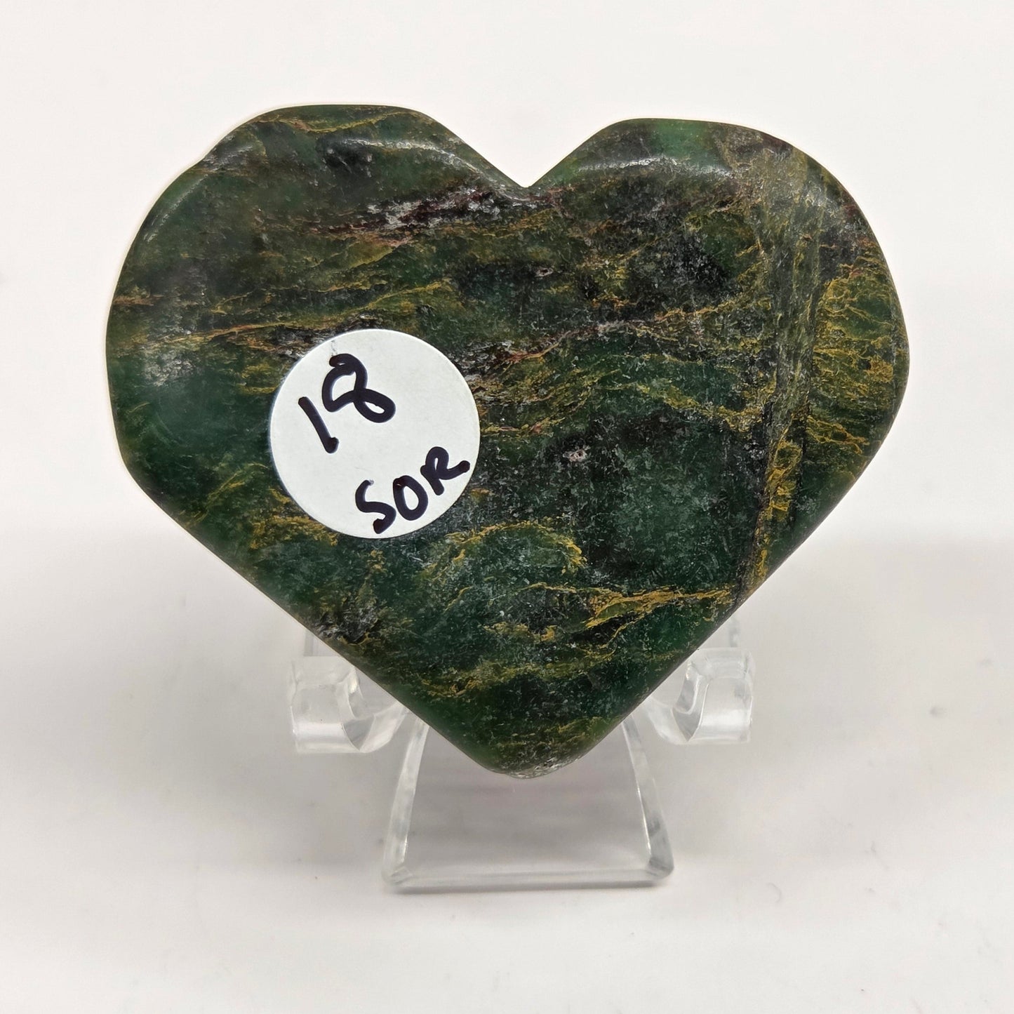 Emerald heart with yellow and black inclusions, on a display stand on a white background