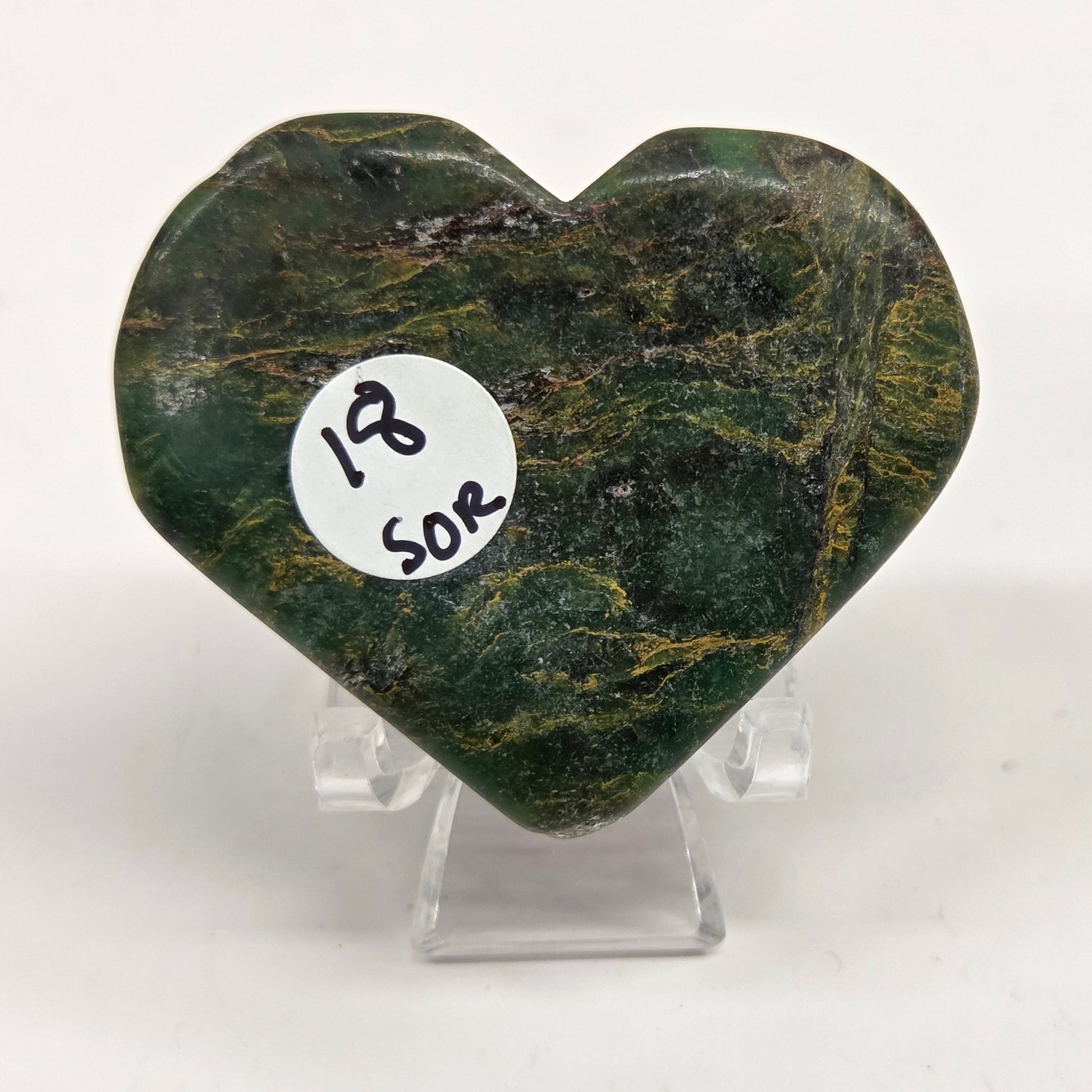 Emerald heart with yellow and black inclusions, on a display stand on a white background