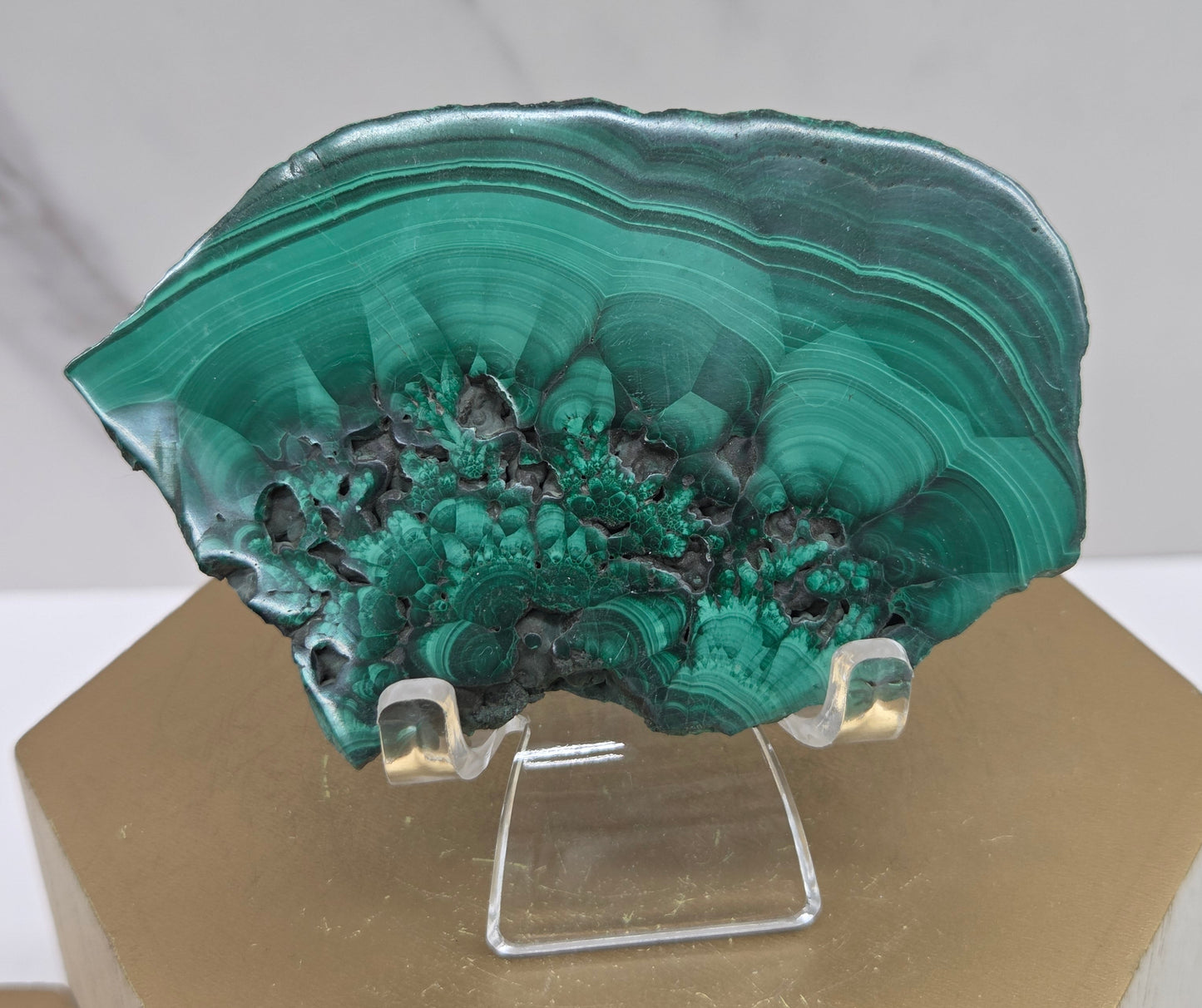 Green malachite crystal on a clear stand with a gold base against a neutral background