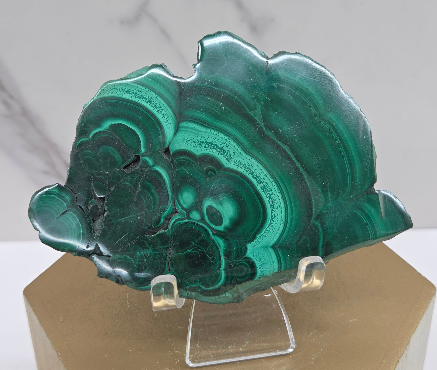 Green malachite crystal on a clear stand against a neutral background