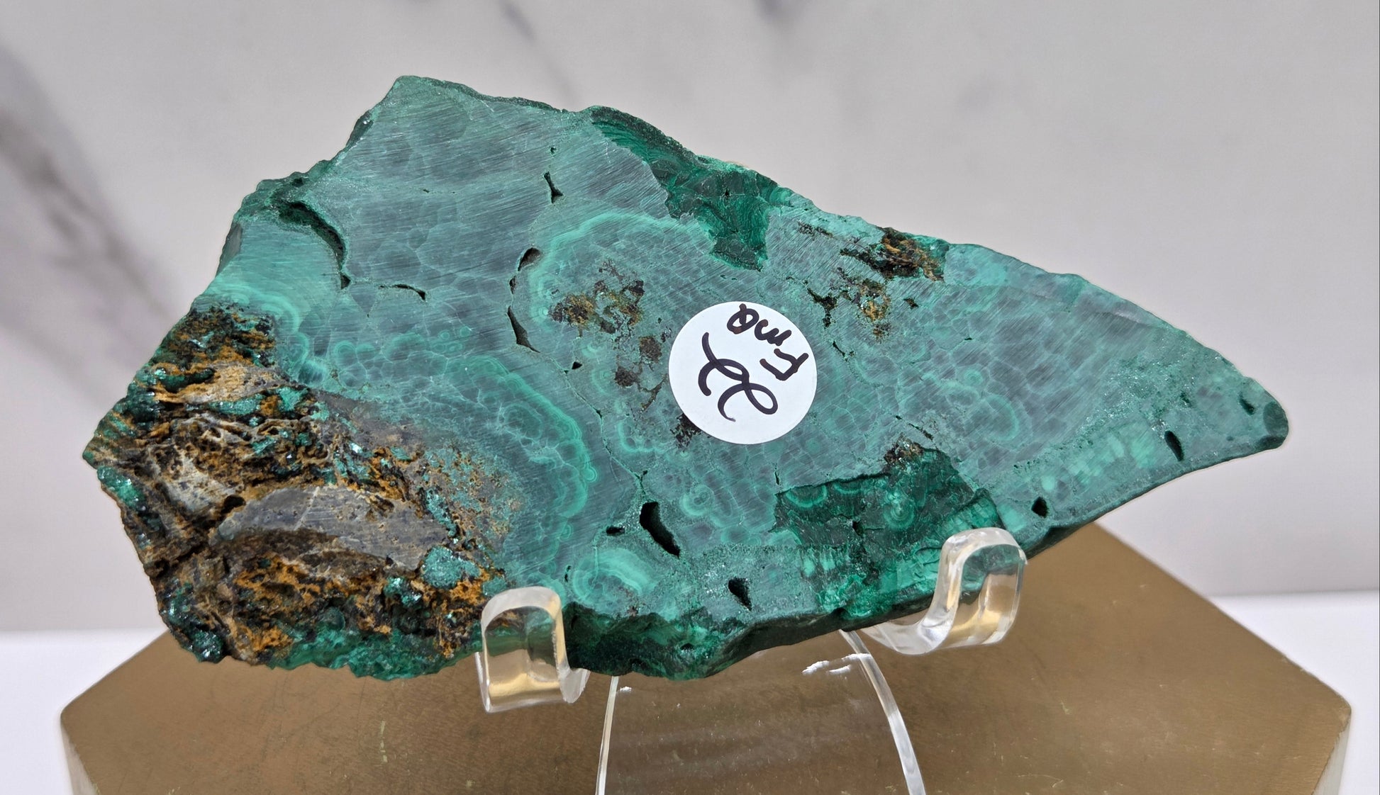 Malachite mineral specimen on a stand with a white label against a marble background