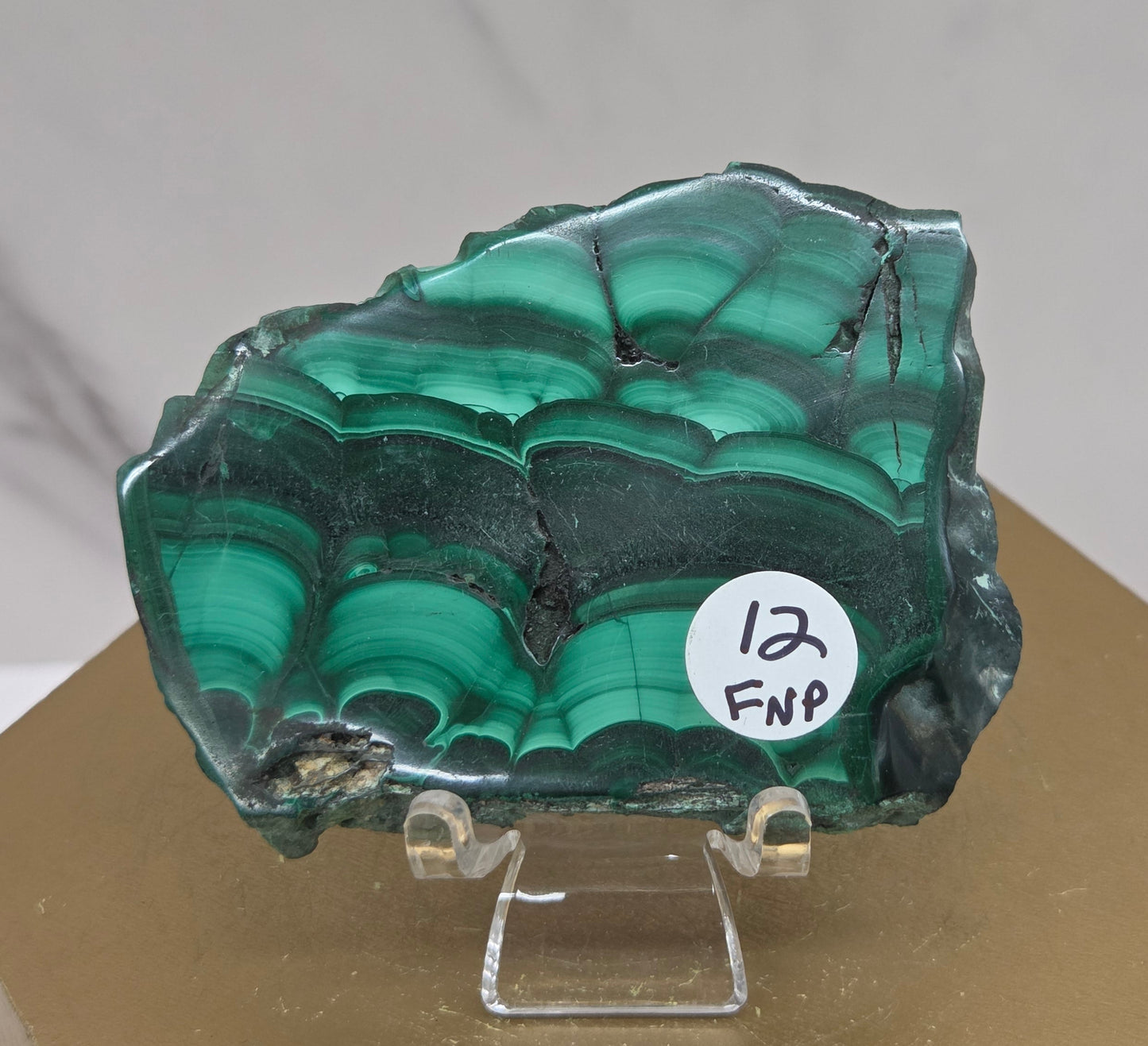 Green malachite crystal on a stand with a label against a neutral background