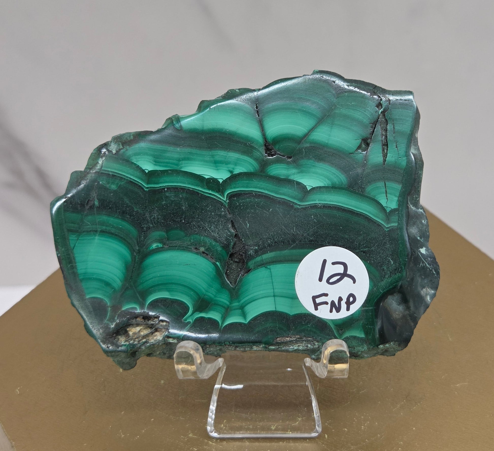 Green malachite crystal on a stand with a label against a neutral background