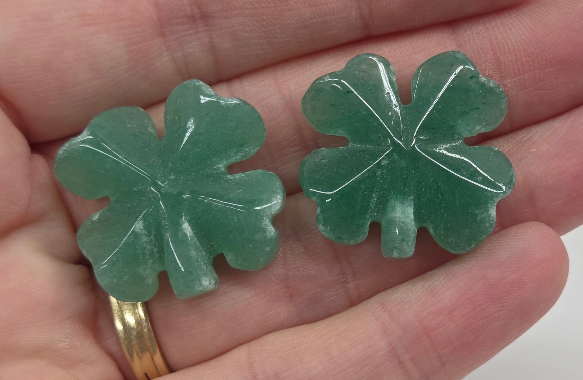Set of green aventurine 4 leaf clover carvings being held in a hand on a white background