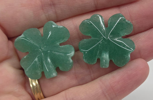 Set of green aventurine 4 leaf clover carvings being held in a hand on a white background