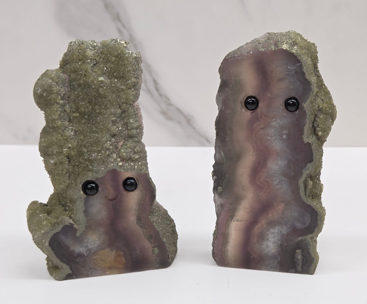 Two fluorite figurines with black eyes on a white surface and marble background