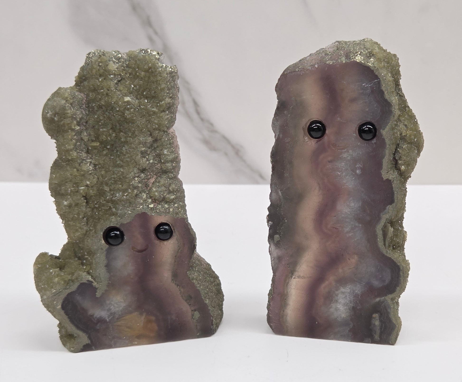Two fluorite figurines with black eyes on a white surface and marble background