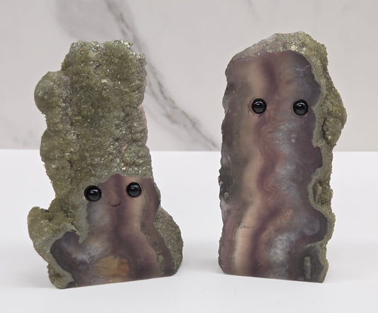 Two fluorite figurines with black eyes on a white surface and marble background