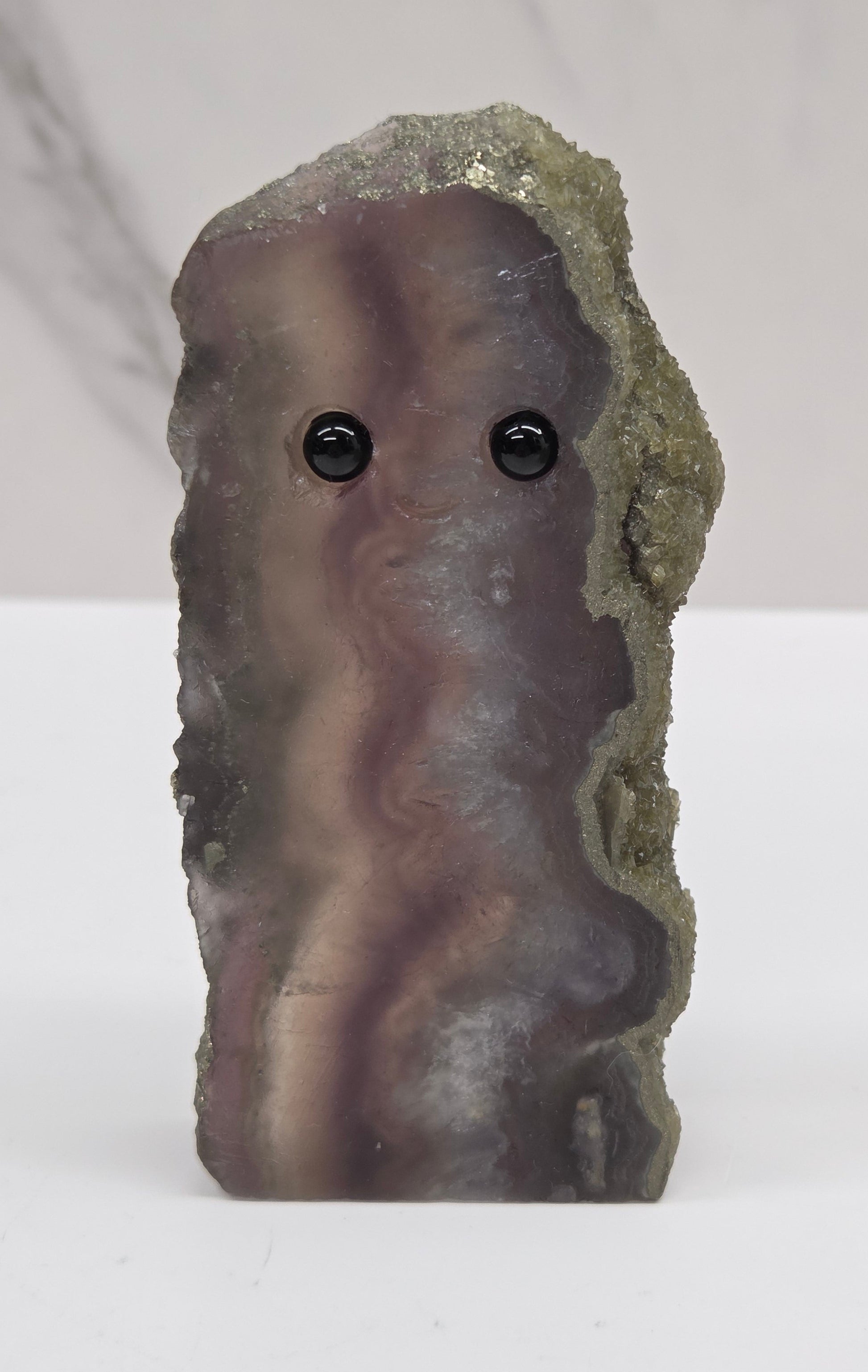 Fluorite figurine with black eyes on a white surface and marble background