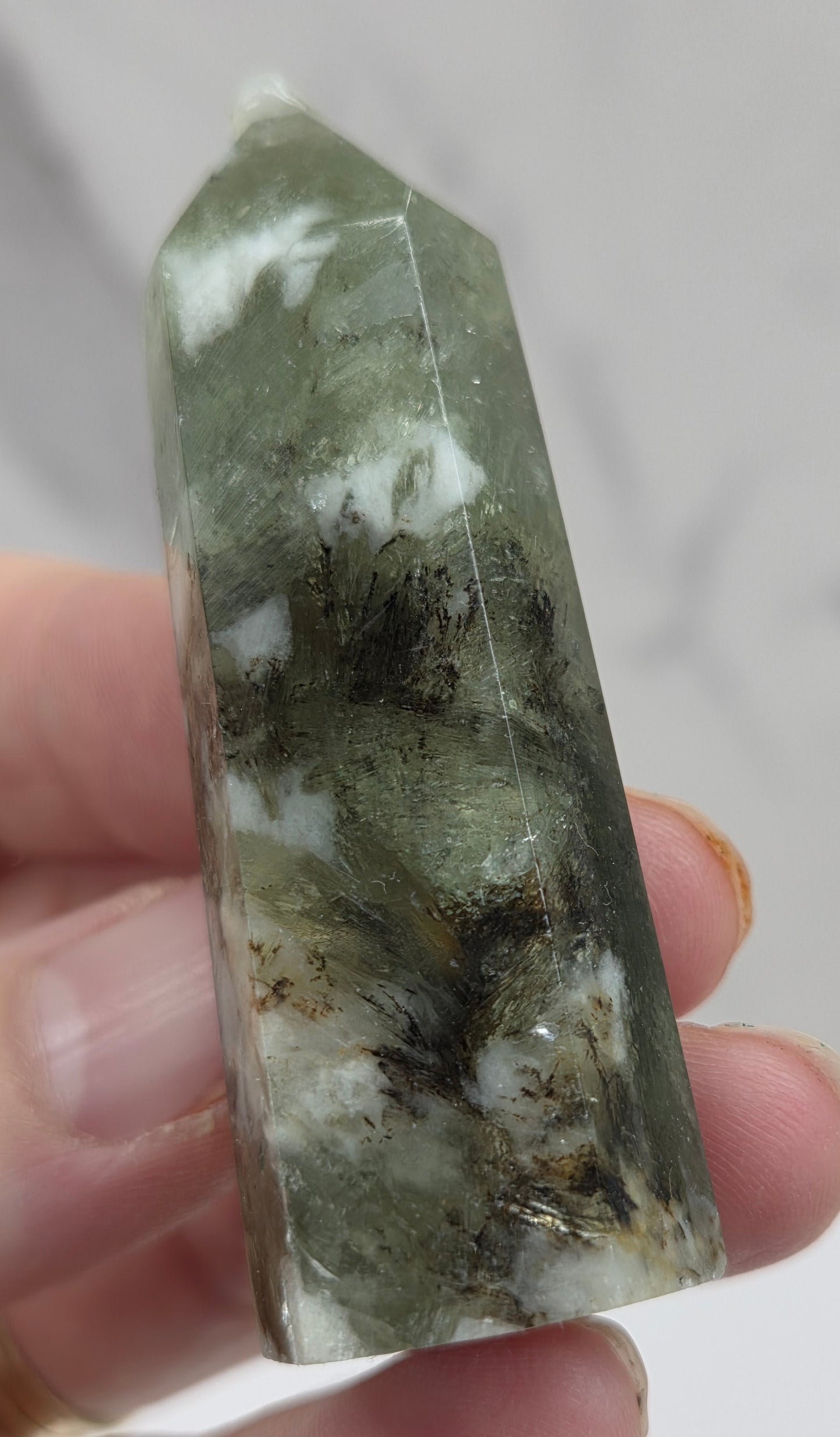 Hand holding a green and white crystal with a blurred background