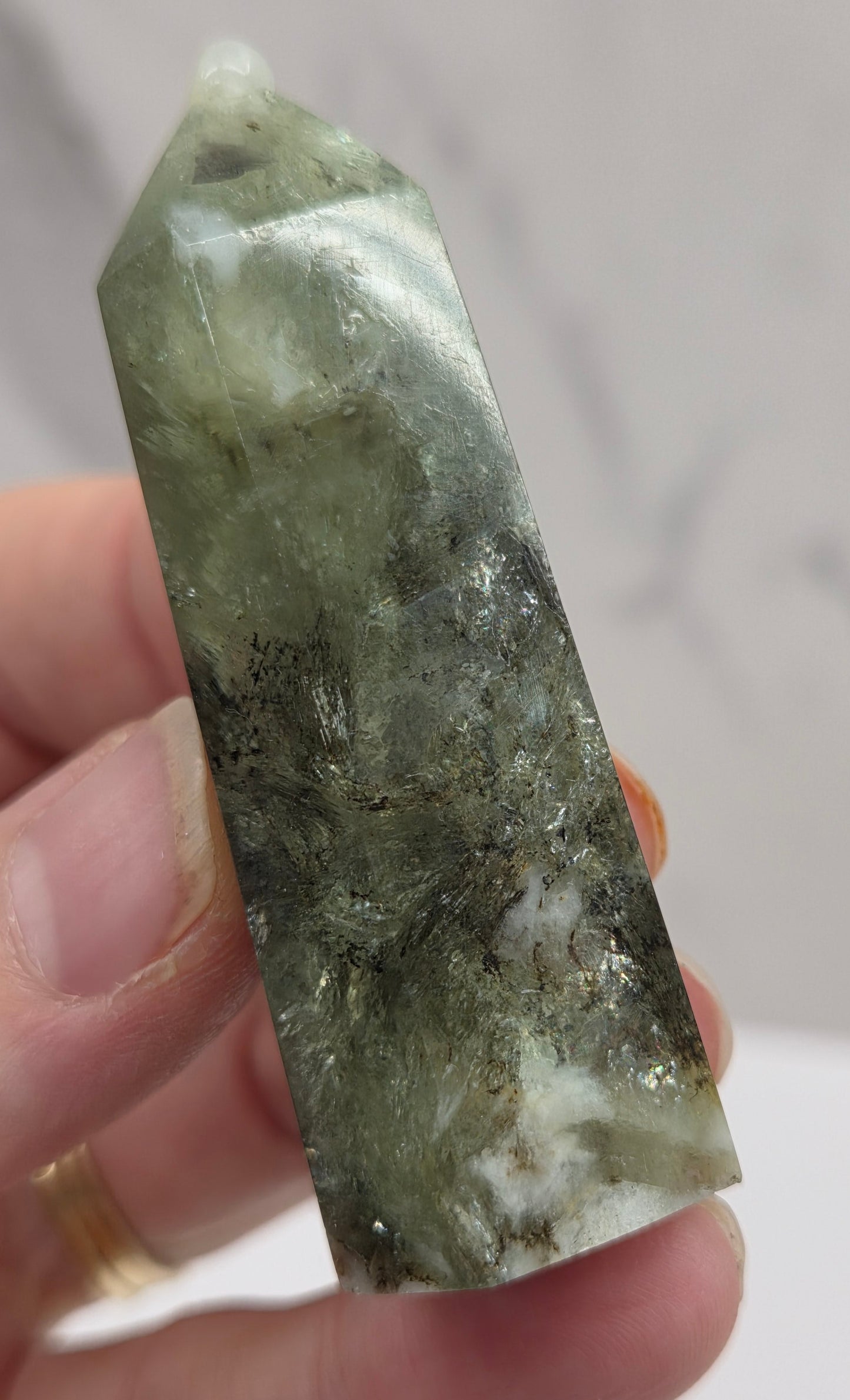 Hand holding a green crystal against a neutral background
