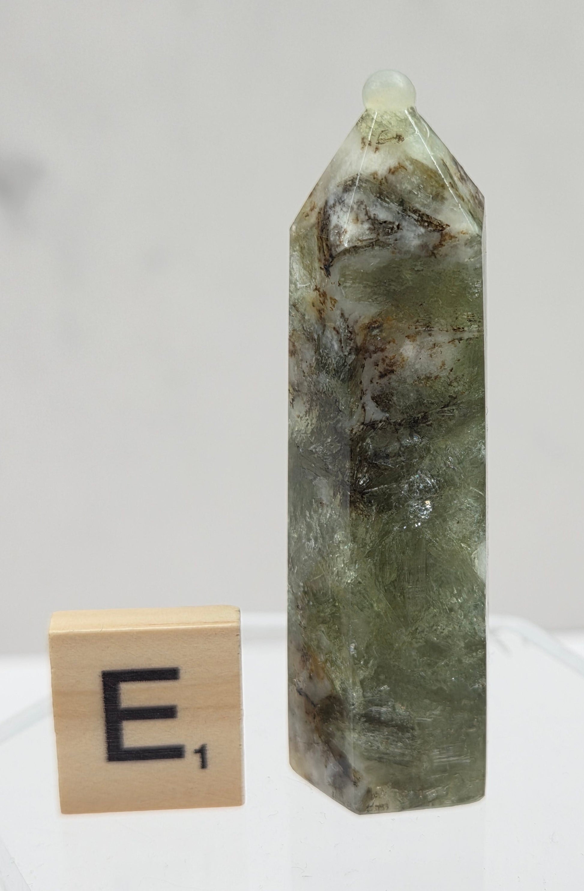 Green crystal on a clear stand with a wooden block labeled 'E' on a white background
