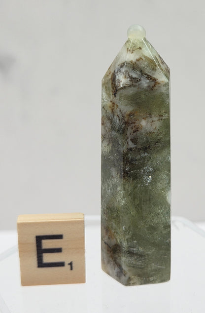 Green crystal on a clear stand with a wooden block labeled 'E' on a white background