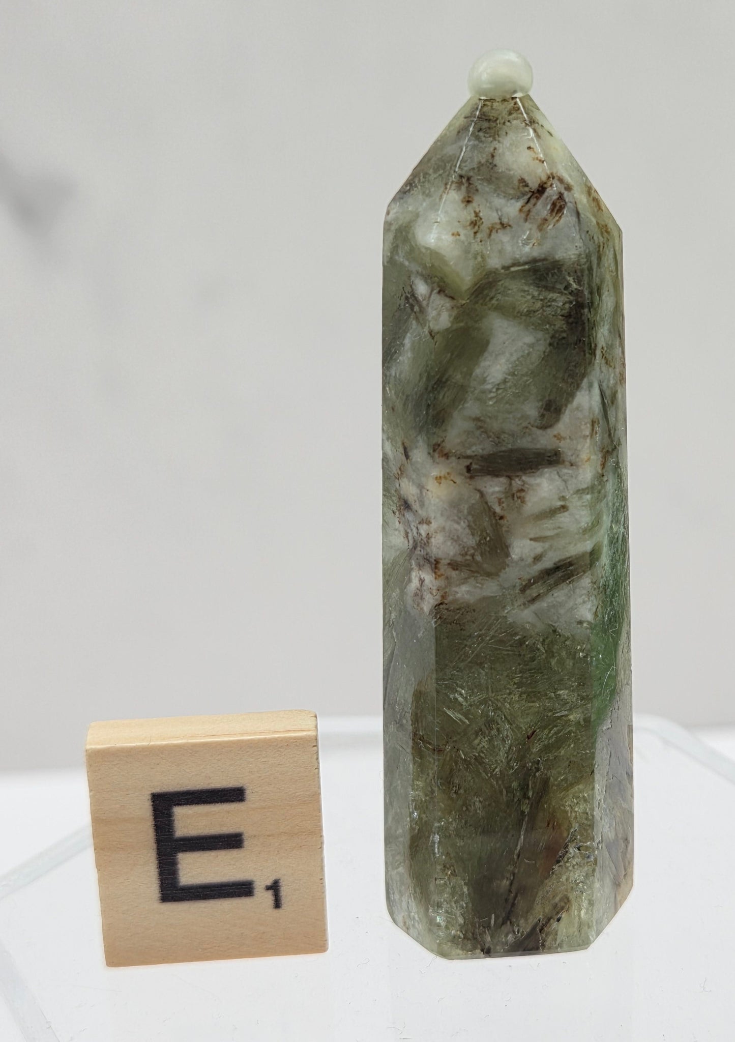 Green crystal on a clear stand with a wooden block labeled 'E' on a white background
