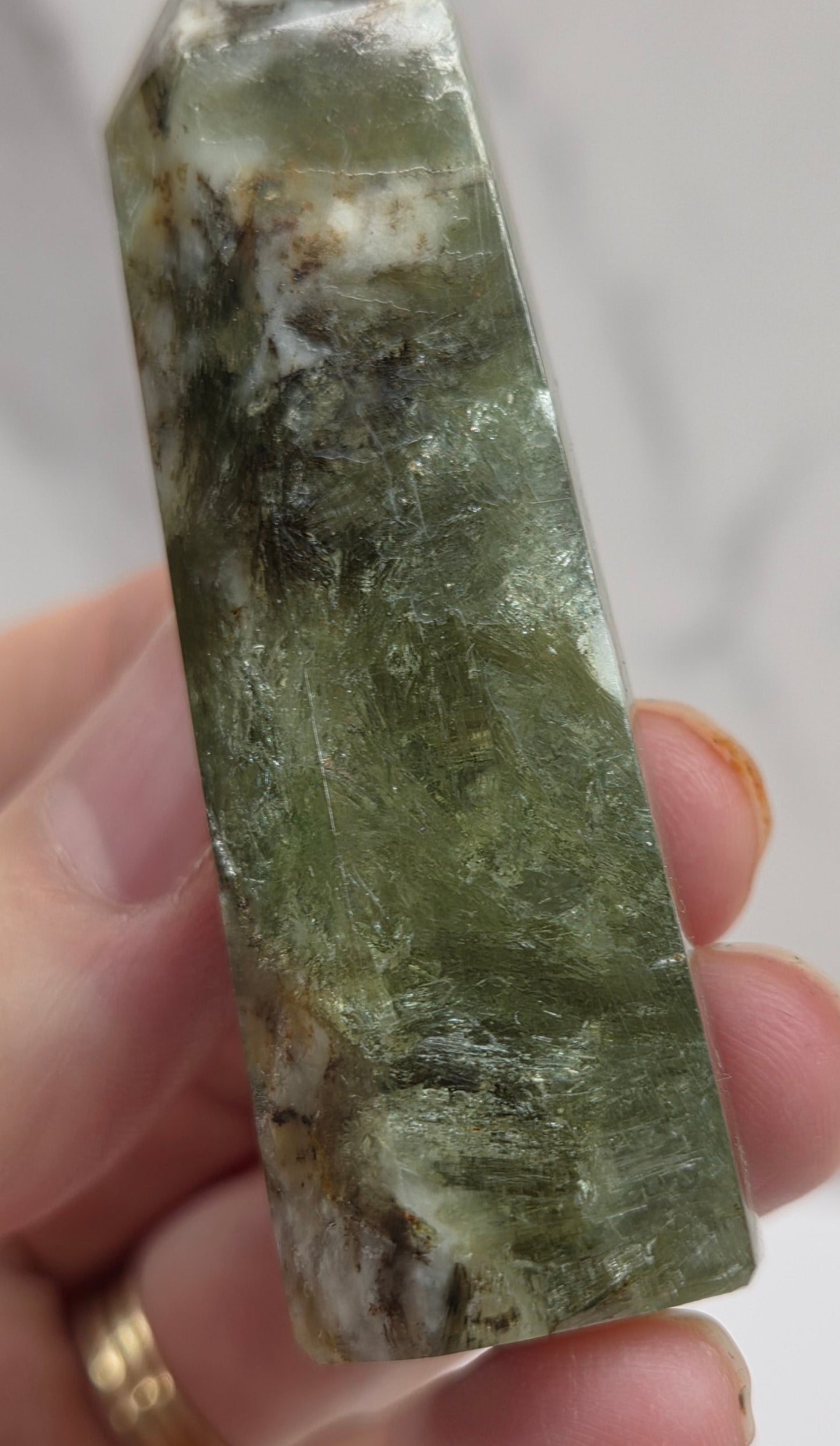 Hand holding a greenish crystal against a white background