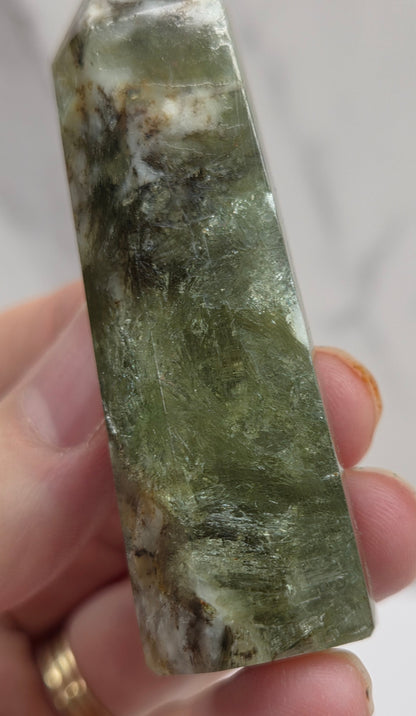 Hand holding a greenish crystal against a white background