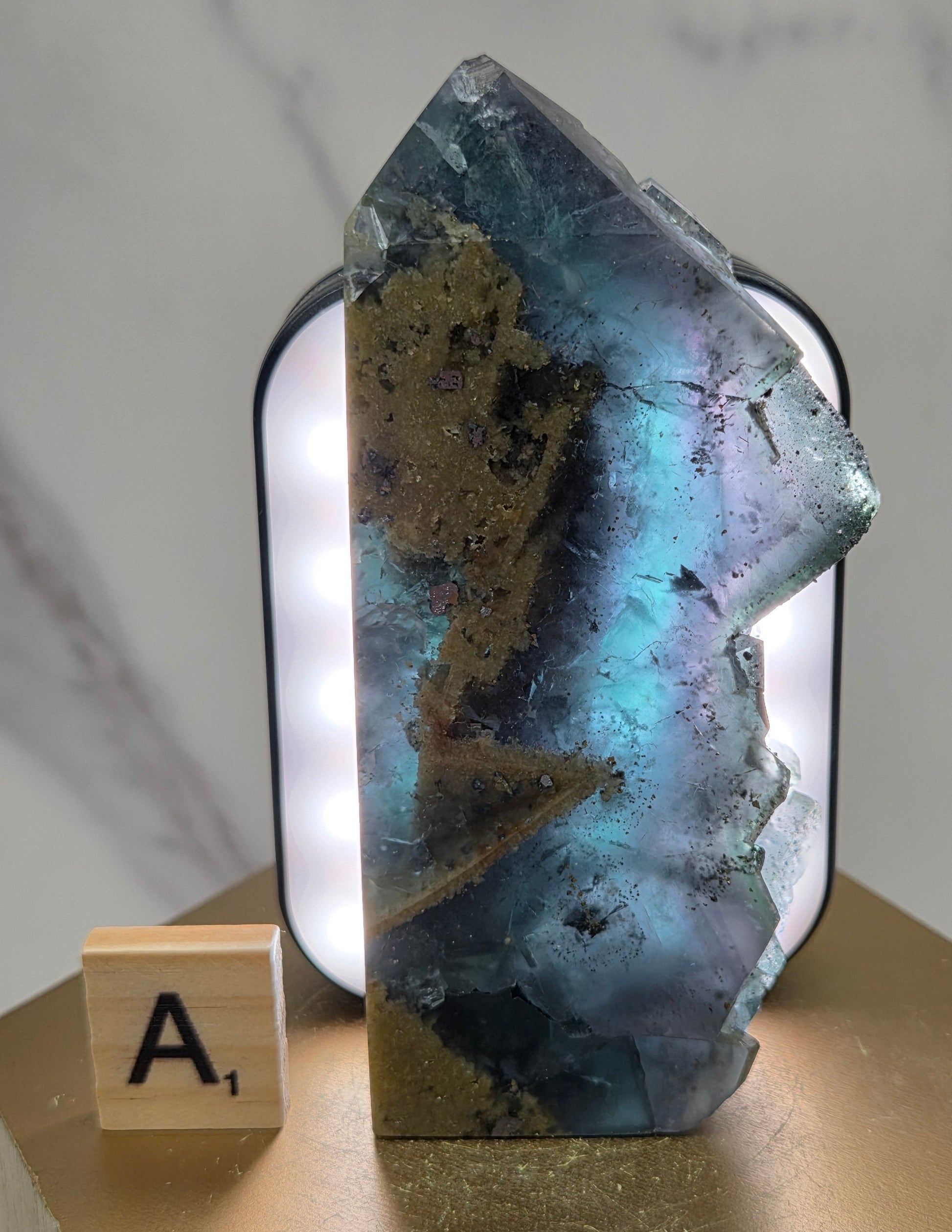 Back-lit Fluorite crystal on a wooden stand with a marble background