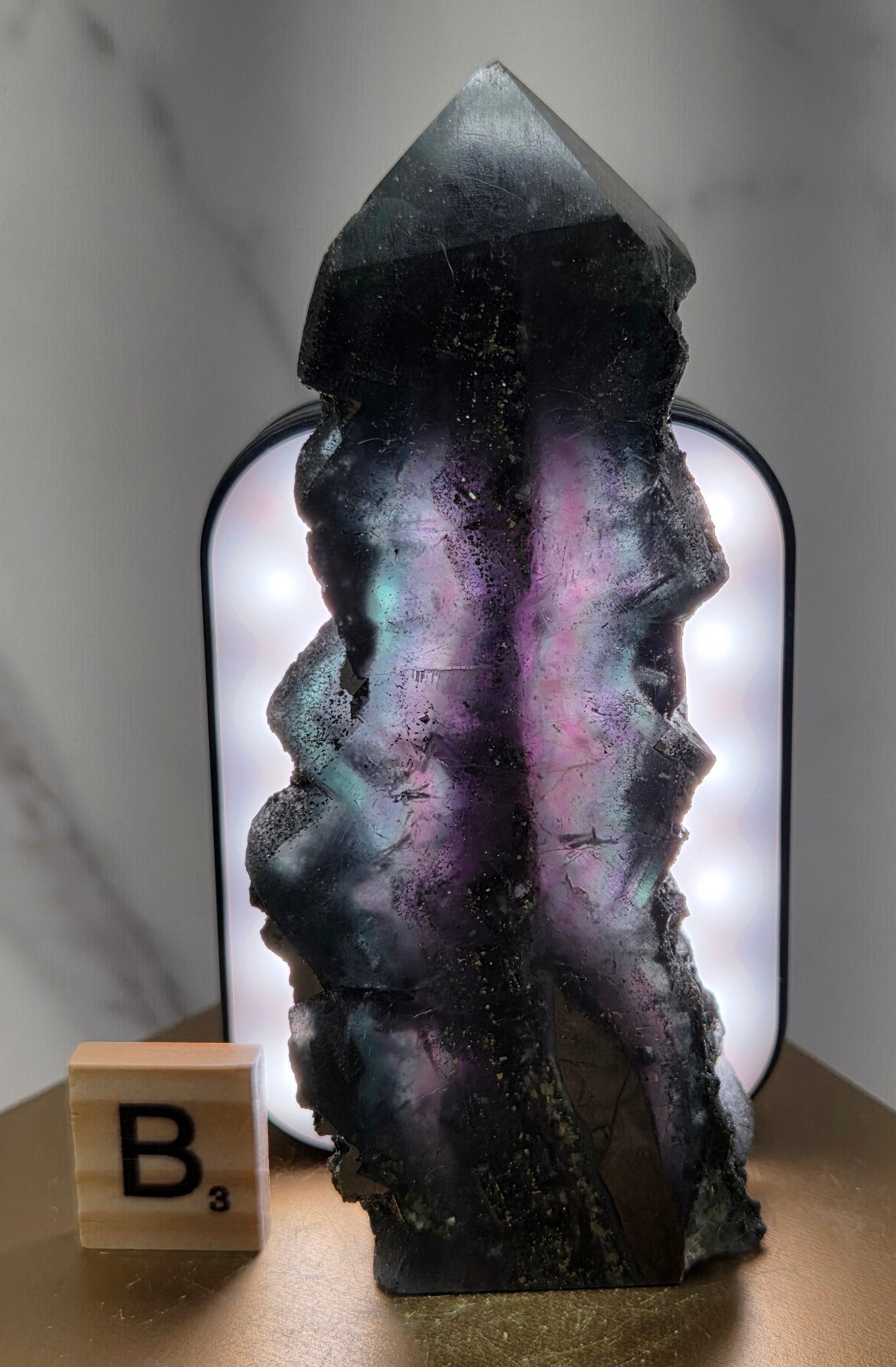 Back-lit Fluorite crystal on a wooden stand with a marble background