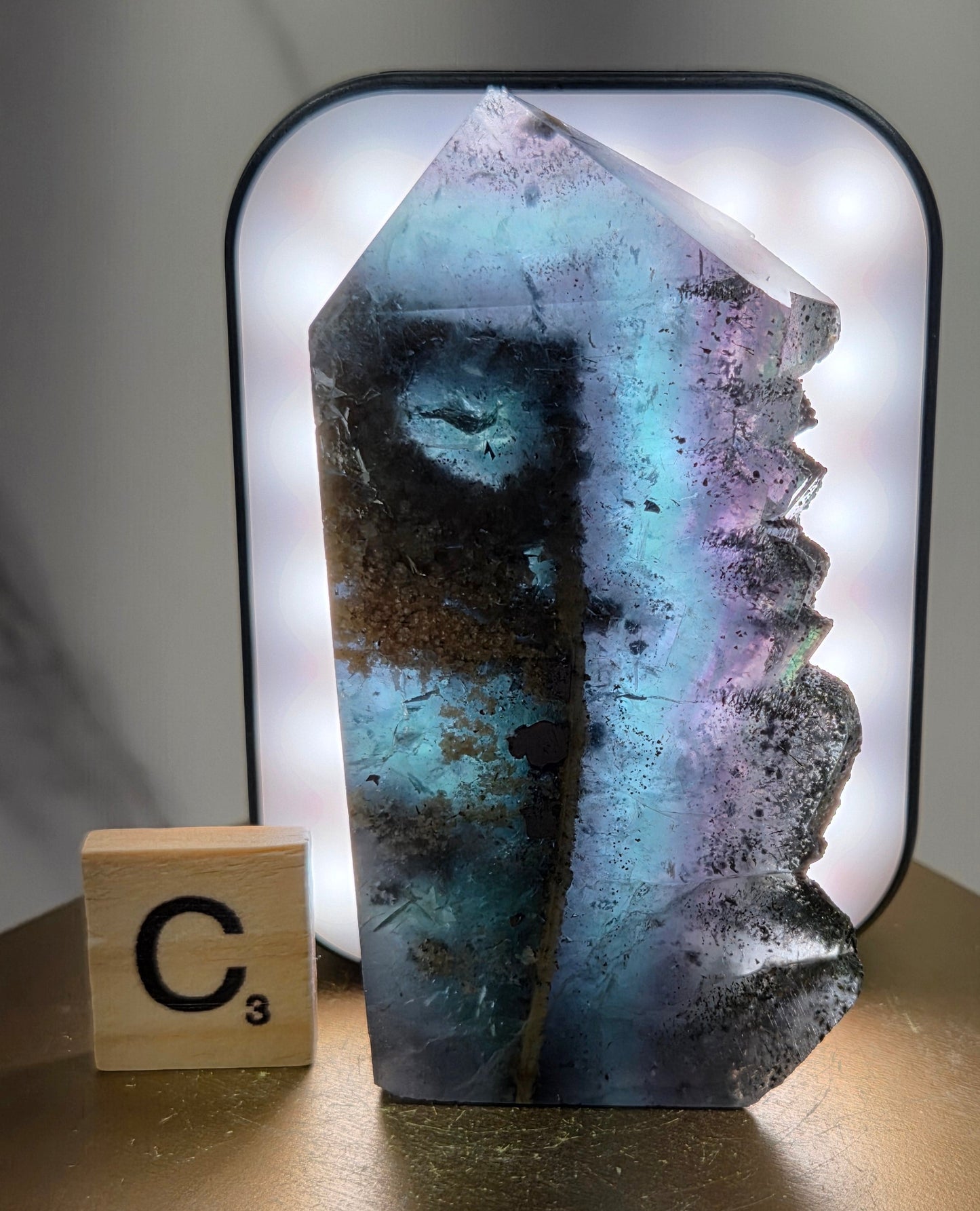 Back-lit Fluorite crystal on a wooden stand with a marble background