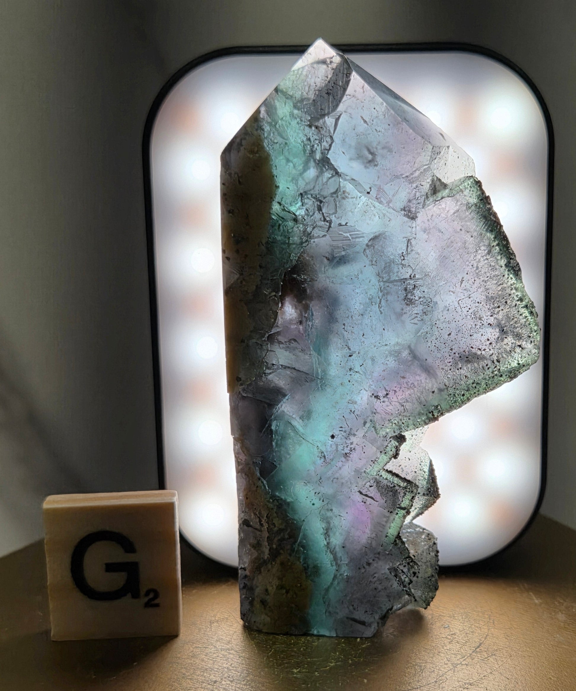 Back-lit Fluorite crystal on a wooden stand with a marble background