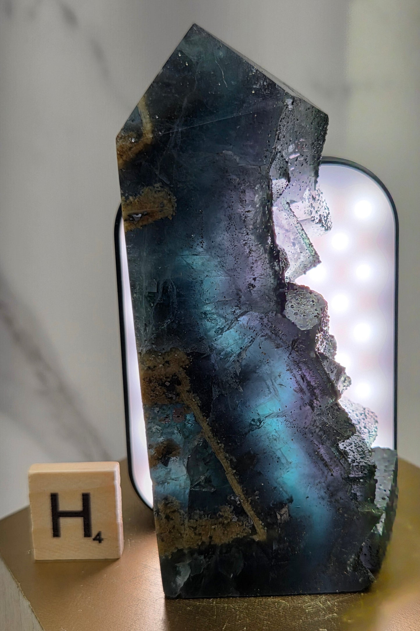 Back-lit Fluorite crystal on a wooden stand with a marble background