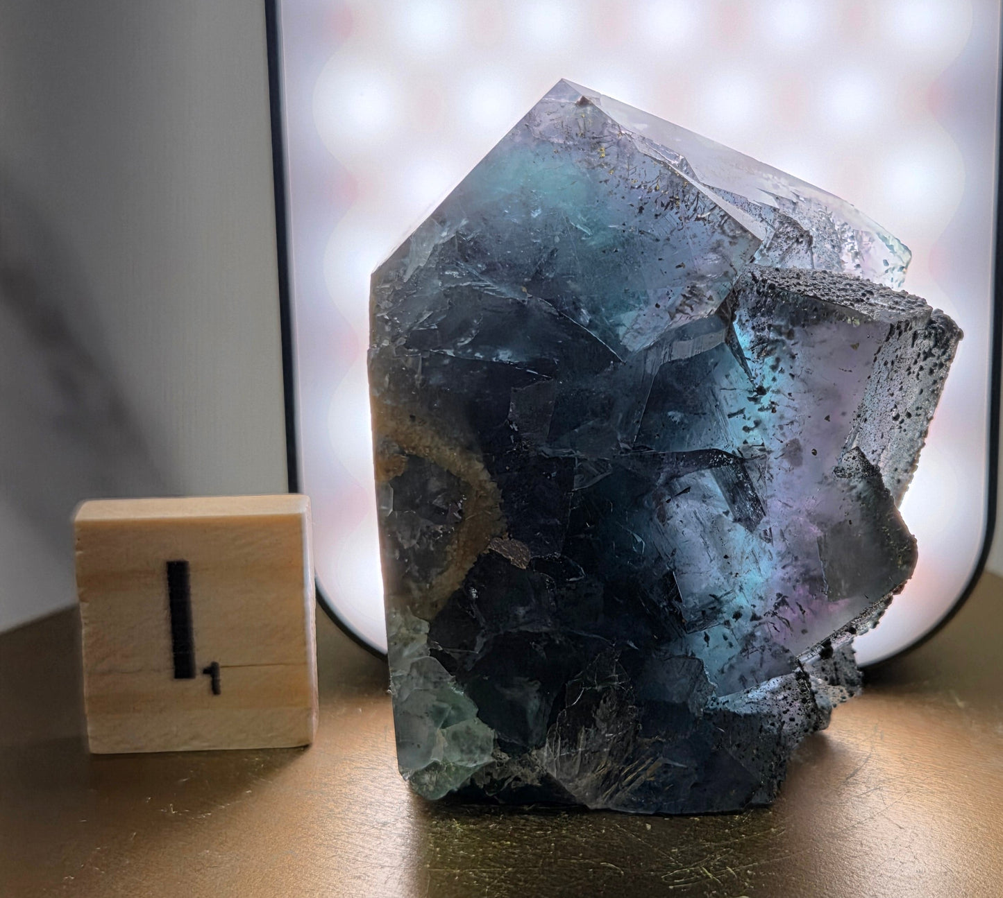 Back-lit Fluorite crystal on a wooden stand with a marble background