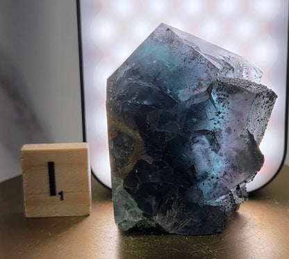 Back-lit Fluorite crystal on a wooden stand with a marble background