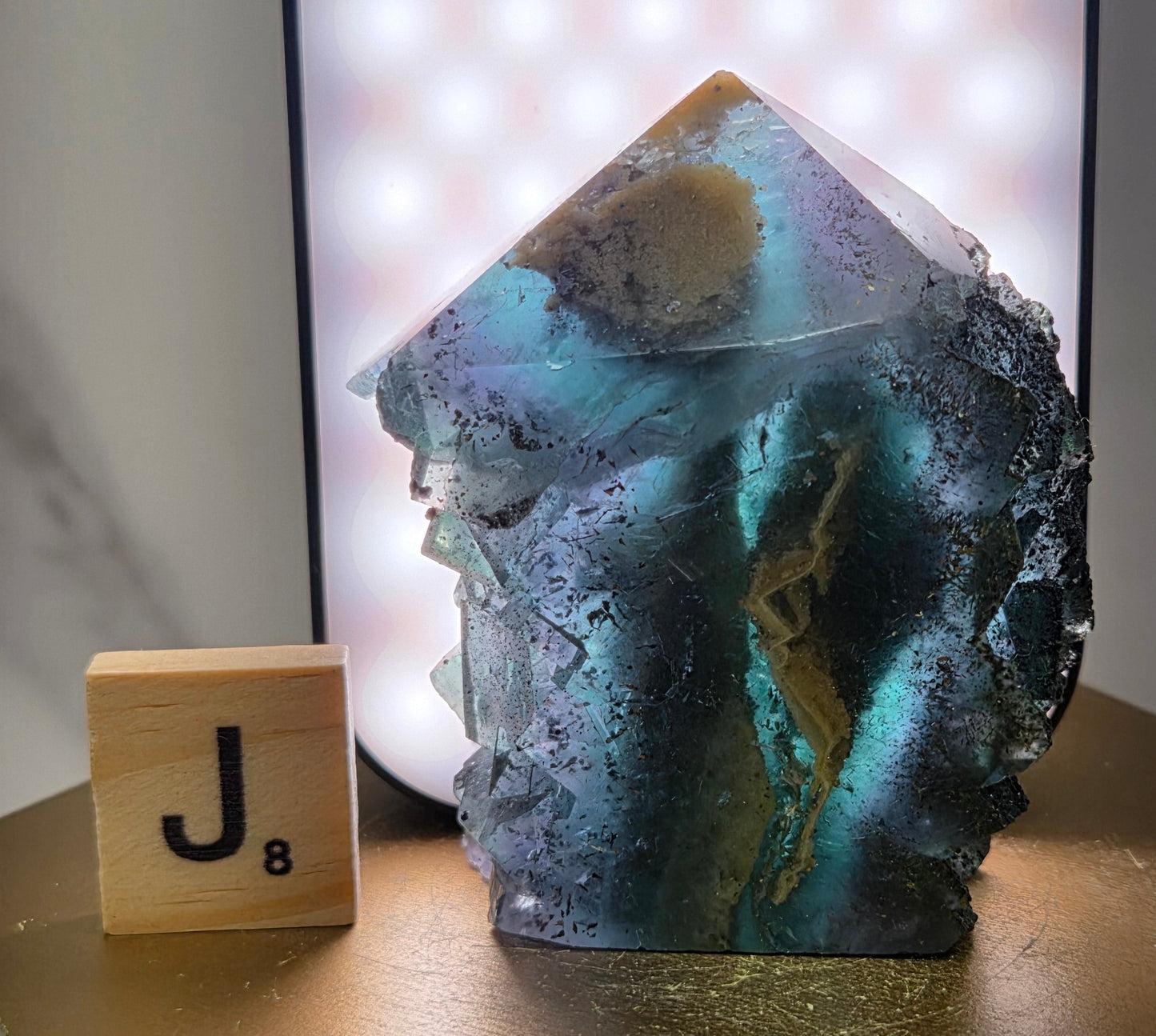 Back-lit Fluorite crystal on a wooden stand with a marble background