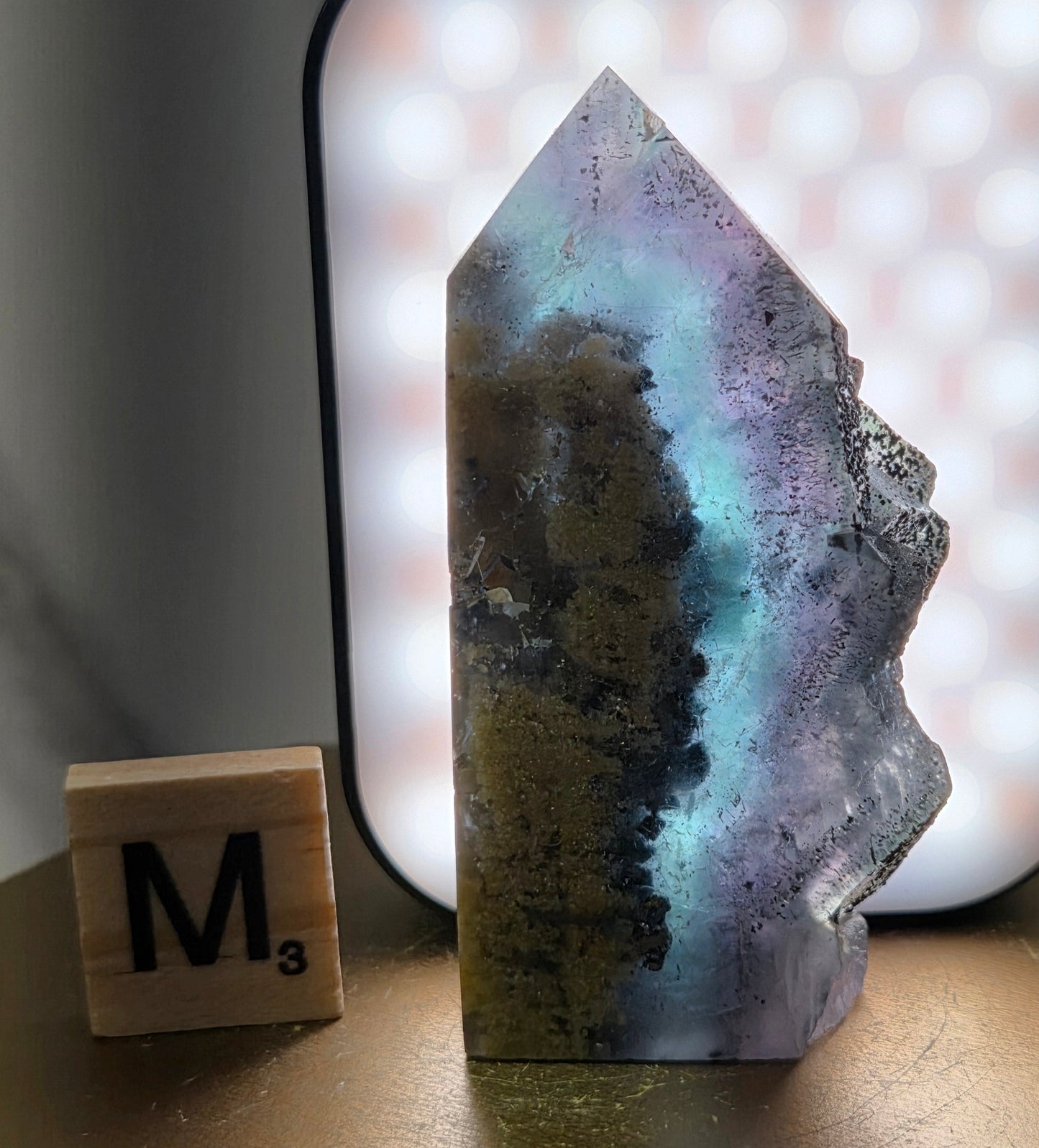 Back-lit Fluorite crystal on a wooden stand with a marble background