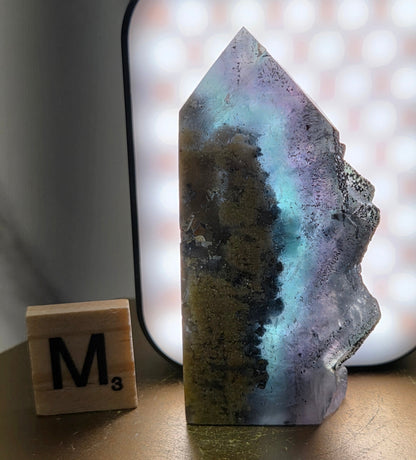 Back-lit Fluorite crystal on a wooden stand with a marble background