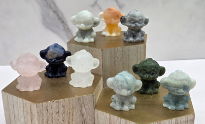 Collection of small crystal monkey figurines on wooden stands against a marble background