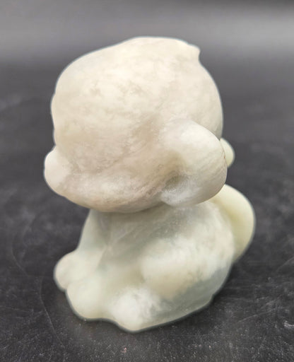 Small calcite monkey carving on a dark surface