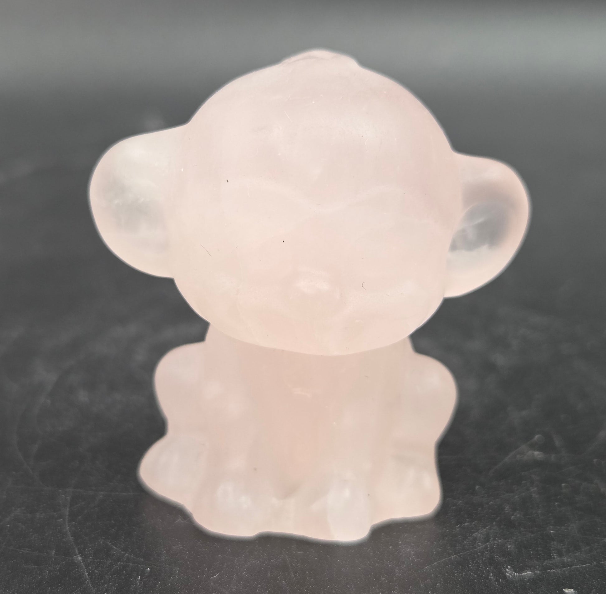 Small pink rose quartz monkey carving on a dark surface