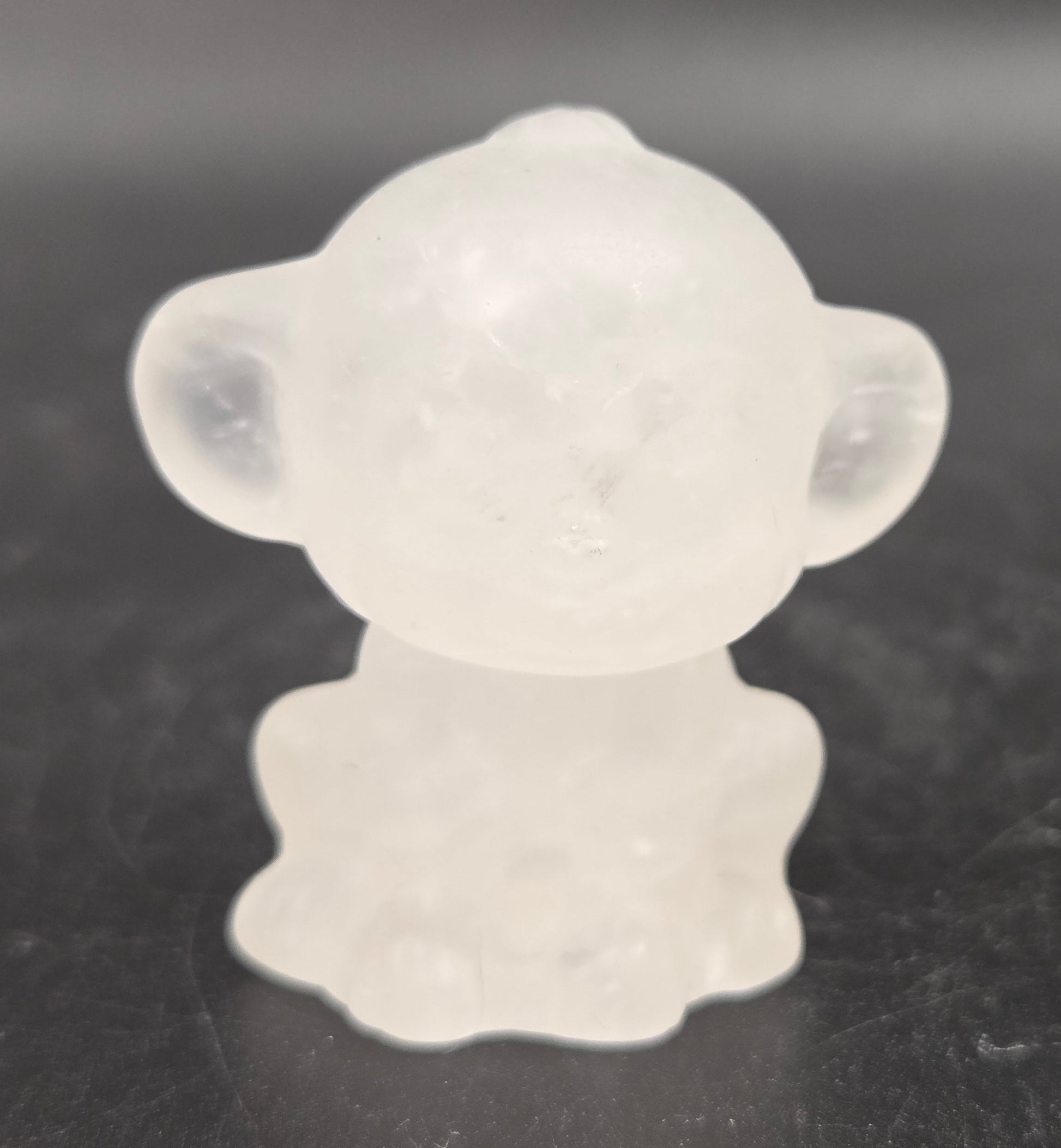 Small clear quartz monkey carving on a dark surface