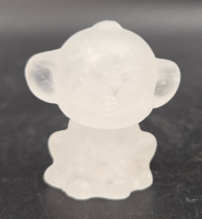 Small clear quartz monkey carving on a dark surface