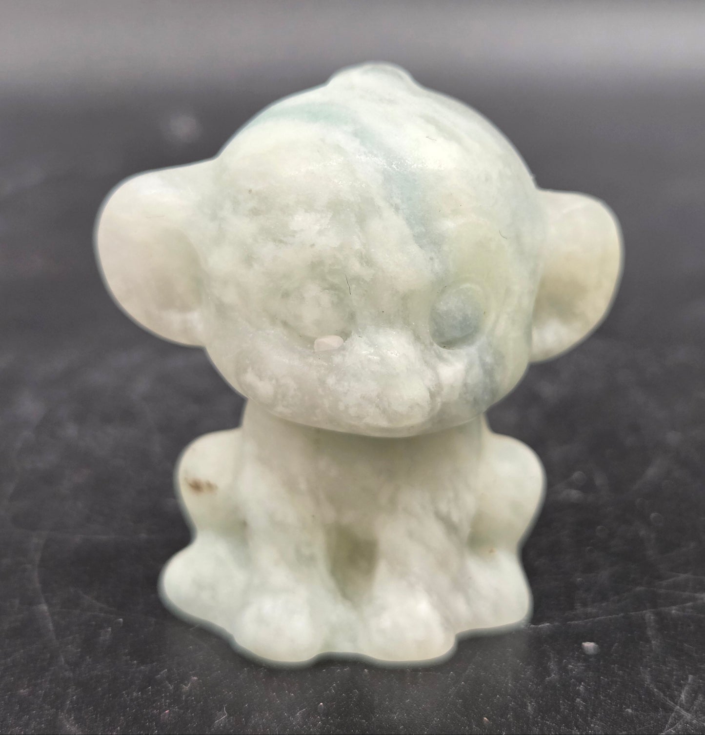 Small calcite monkey carving on a dark surface