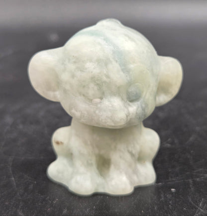 Small calcite monkey carving on a dark surface