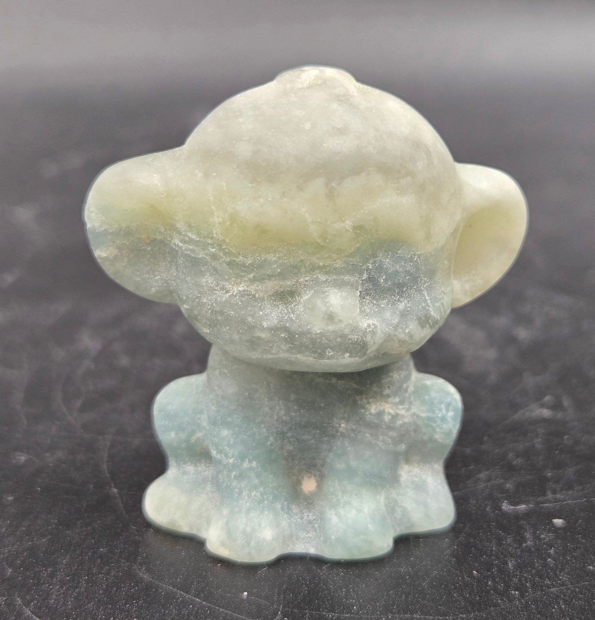 Small calcite monkey carving on a dark surface